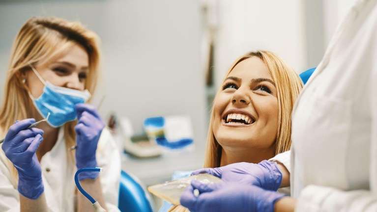 female patient smiling in dental chair while dentist looks on