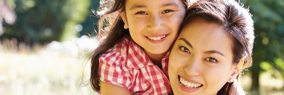 Mother and daughter smiling hugging in field